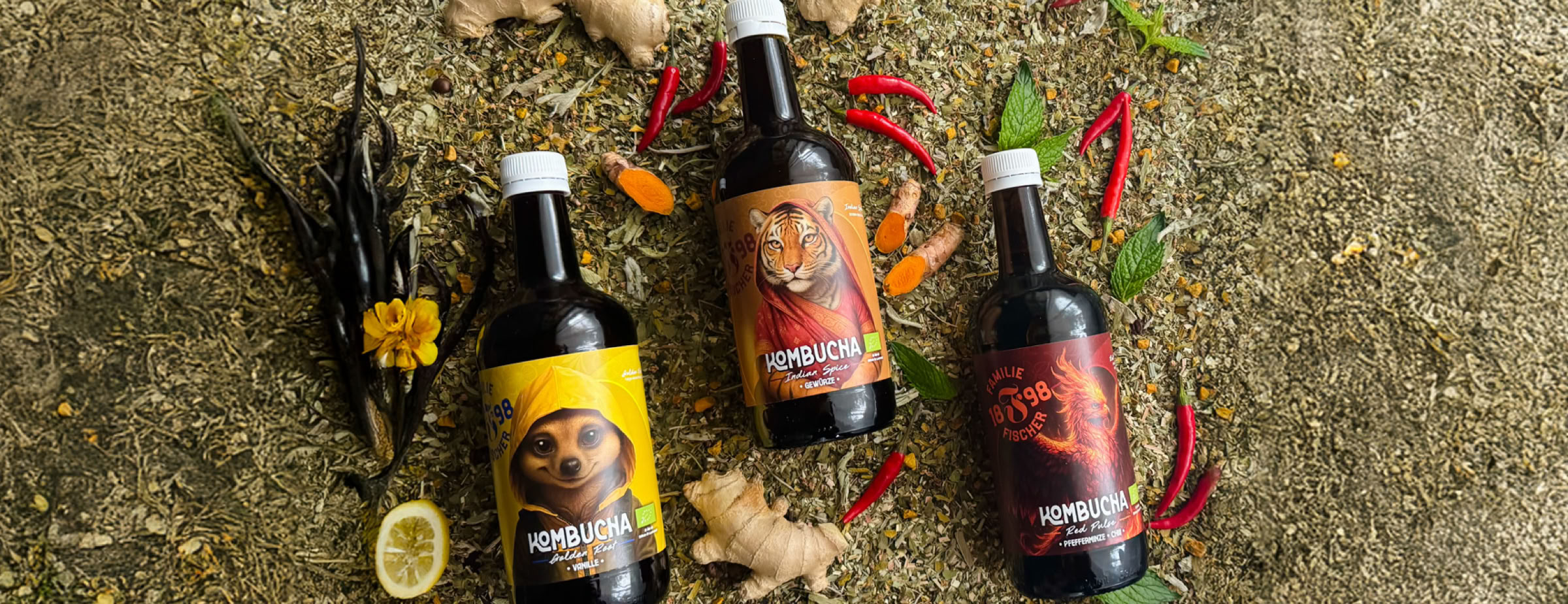 Drei Flaschen mit bunten Etiketten liegen auf einem Boden, umgeben von Chilischoten, Vanilleschoten und einer Zitronenscheibe.