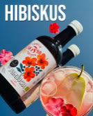 Zwei Flaschen mit Hibiskus-Etikett, ein Glas mit Getränk, Eiswürfeln, einer Birnenscheibe und Hibiskusblüten vor blauem Hintergrund.