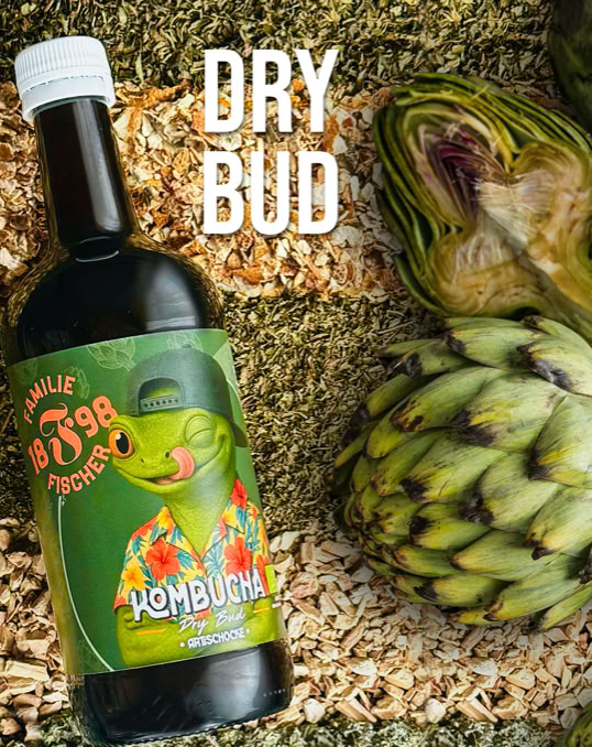 Eine Flasche mit einem Etikett, das eine grüne Cartoon-Figur in einem Hawaii-Hemd zeigt, steht auf einer Mischung aus getrockneten Pflanzen. Daneben liegt eine Artischocke. Oben steht der Text "DRY BUD".